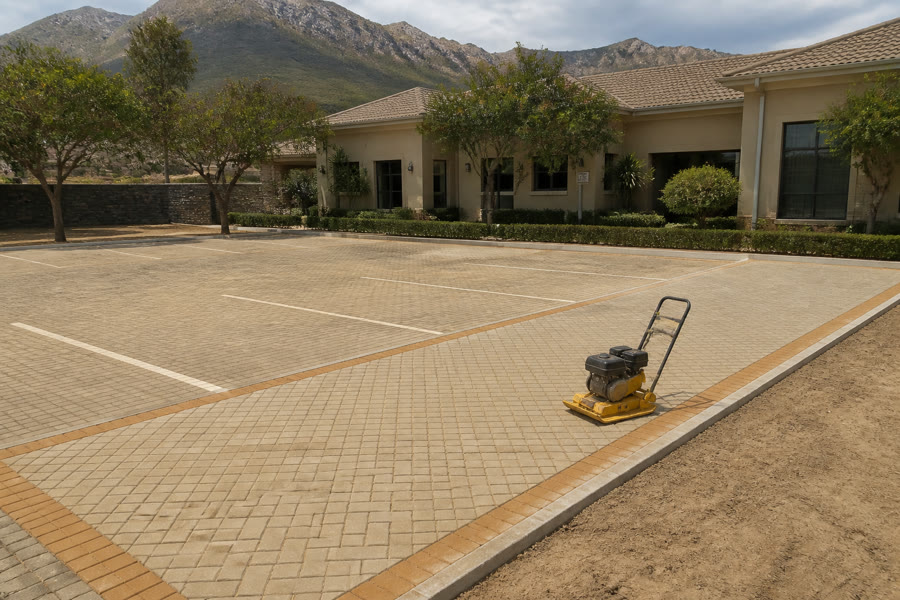 Warm sand-beige visitor parking field with ochre borders and plate compactor at a Somerset West Helderberg complex.
